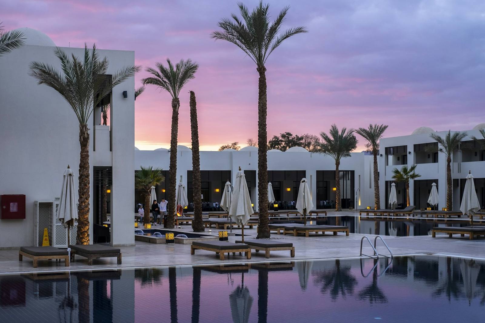 A resort pool lined with palm trees at dusk