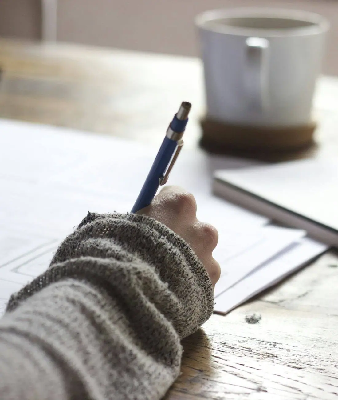Hands writing notes beside a cup of coffee