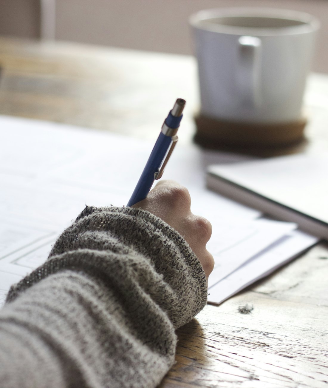 Hands writing notes beside a cup of coffee